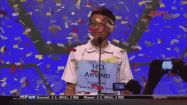 a boy with the number 163 on his shirt stands in front of a microphone with confetti falling around him