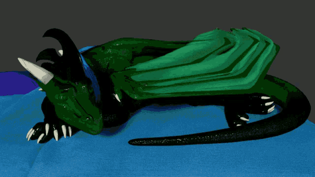 a green dragon is laying down on a blue cloth