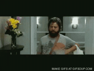 a man with a beard is standing in front of a vase of flowers and says make gifs at gifsoup
