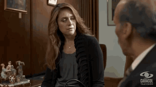 a woman is sitting at a desk talking to a man in a suit .
