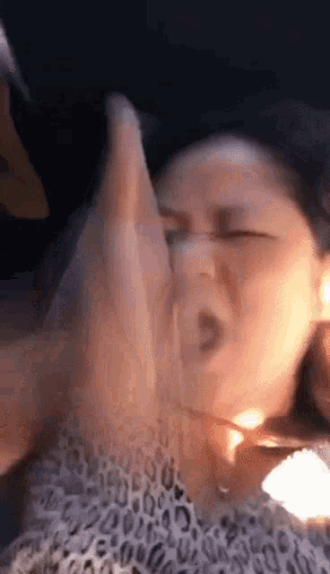 a woman in a leopard print shirt is making a funny face with her hands in front of her face .