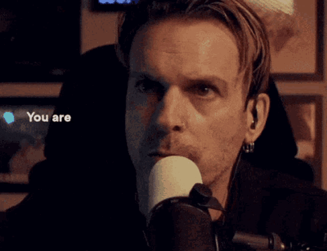 a man is smiling in front of a microphone with the words " you are " next to him