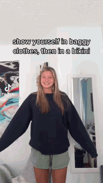 a woman is standing in front of a mirror wearing a black sweater and green shorts and a tiktok video .