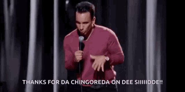 a man in a red shirt is standing on a stage holding a microphone and making a funny face .