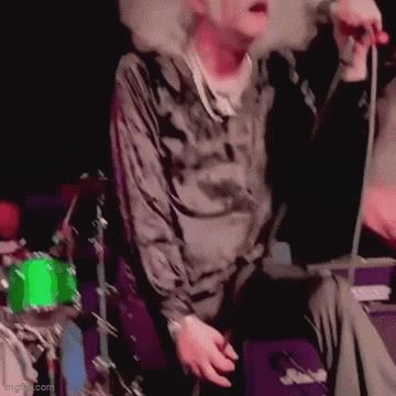 a man is smoking a cigarette and singing into a microphone while sitting on a stage .