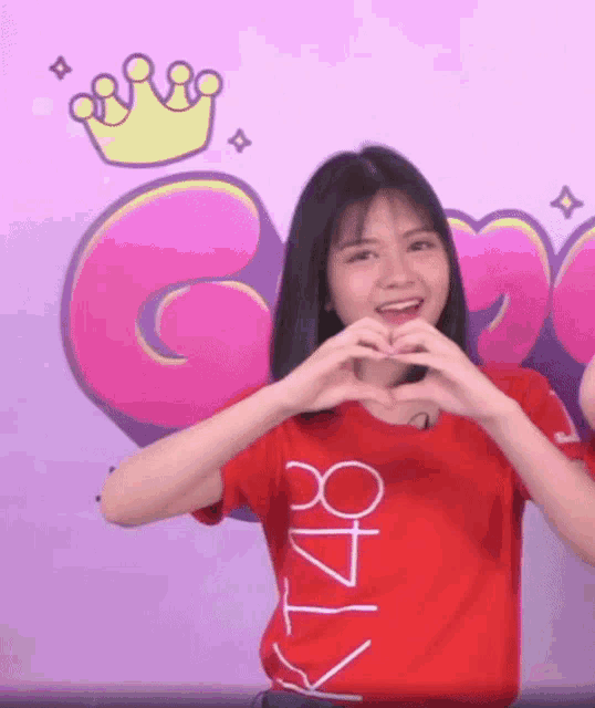 a girl wearing a red shirt that says kt48 makes a heart with her hands