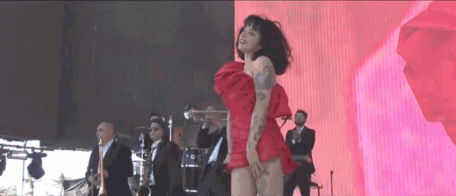 a woman in a red dress is dancing on stage with a band behind her
