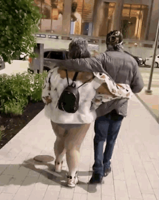 a man and a woman are walking down a sidewalk and the woman has a backpack on her back
