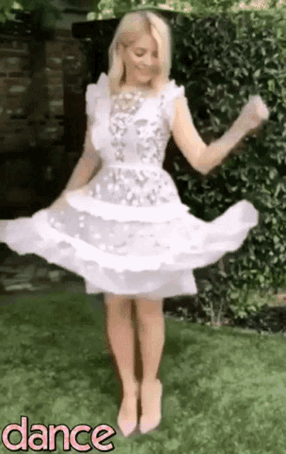 a woman in a white dress is dancing on the grass in a garden .