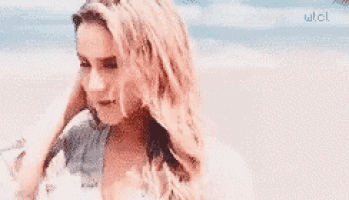 a woman is standing on a beach with her hair blowing in the wind