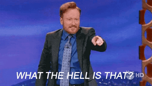 a man in a suit and tie is pointing at the camera and says what the hell is that ?