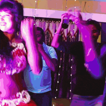 a group of people are dancing in a room with purple lights hanging from the ceiling