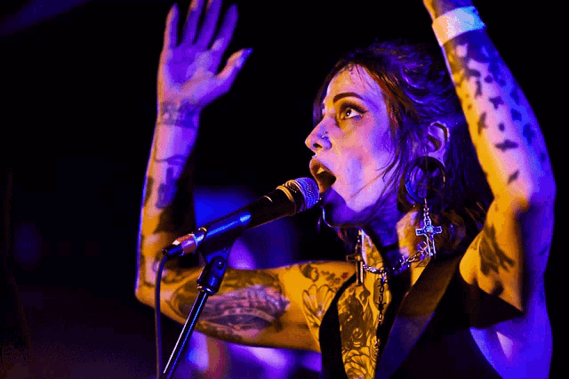 a woman with tattoos singing into a microphone with her hands in the air