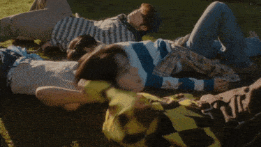 a group of young men laying on the grass with one wearing a plaid shirt