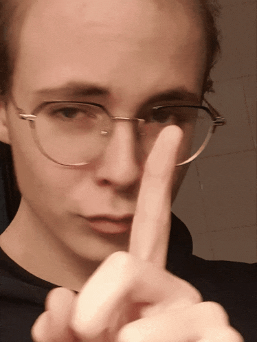 a man wearing glasses and a black shirt is pointing his finger at the camera
