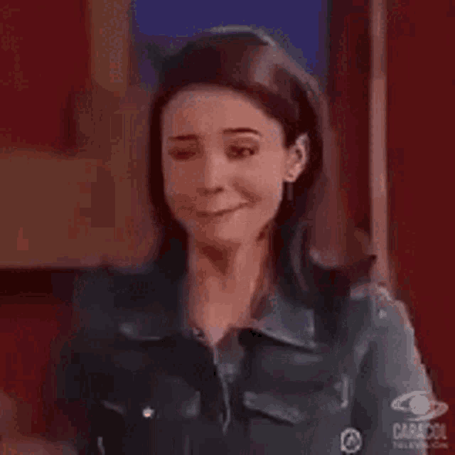 a woman in a denim jacket is smiling while standing in a room .
