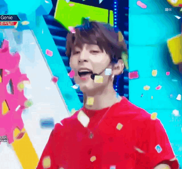 a man in a red shirt is standing on a stage with confetti falling around him