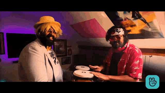 two men are playing drums in a room with a peace sign on the bottom right
