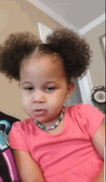 a little girl is wearing a pink shirt and a necklace
