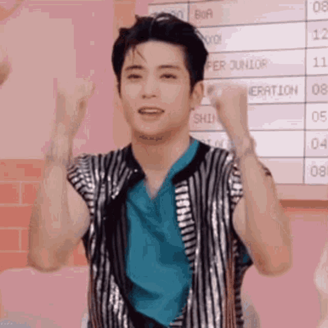 a young man is standing in front of a pink wall with his arms raised in the air .