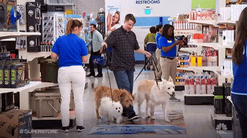 a man is walking two dogs in a store with a sign that says restrooms in the background .