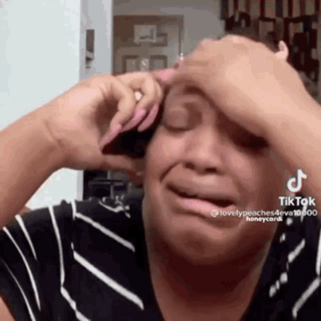 a woman is crying while talking on a cell phone and covering her face with her hand .