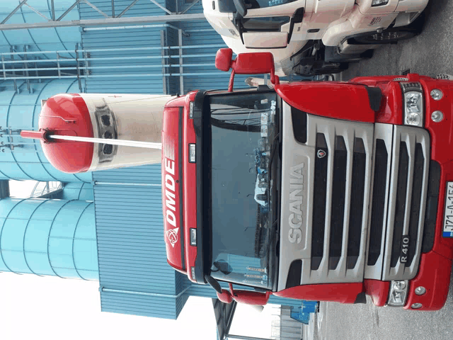 a red and silver scania truck is parked in front of a building