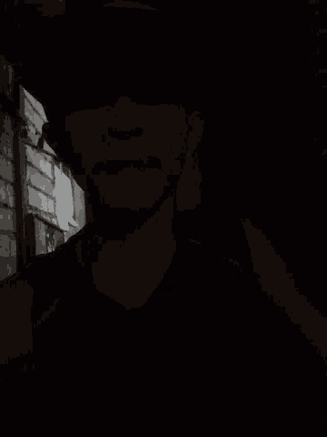 a man in a black hat is laying down in the dark with his eyes closed
