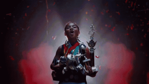 a woman is holding a trophy in her hands in a dark room with confetti falling around her .