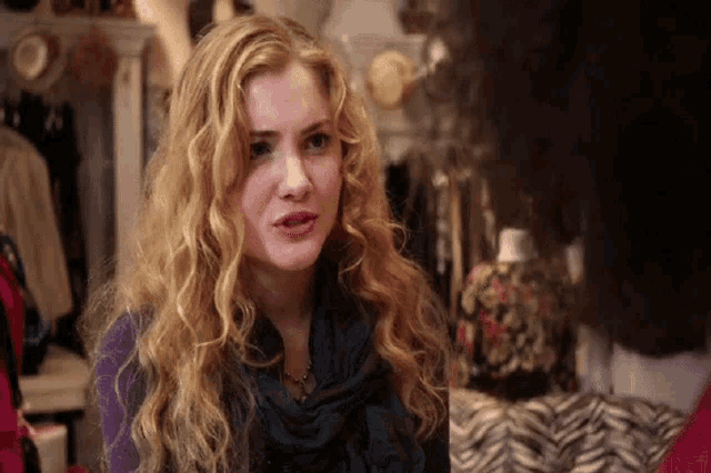 a woman with blonde curly hair is wearing a blue scarf and a purple sweater