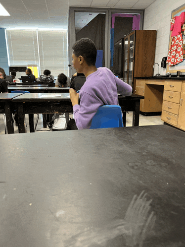 a boy sits at a desk in a classroom with other students