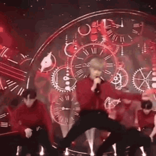 a group of people are dancing on a stage with a clock in the background .