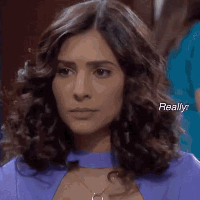 a woman with curly hair is wearing a purple top and necklace and says " really "