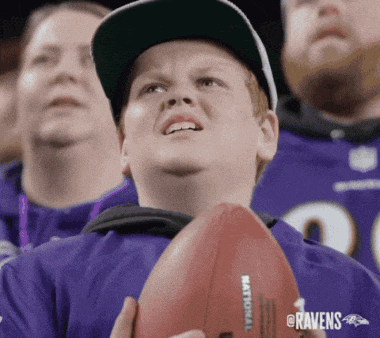 a ravens fan holds a football in front of a crowd