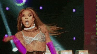 a drag queen wearing a bra and gloves is dancing on stage .