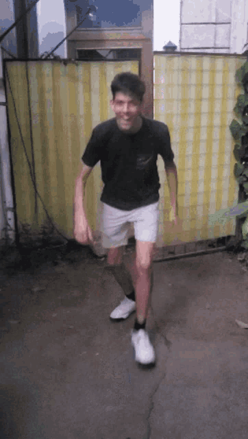a young man wearing a black shirt and white shorts is standing in front of a yellow and white striped curtain