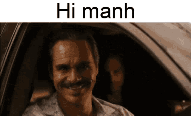 a man with a mustache is smiling in a car and the words hi manh are above him