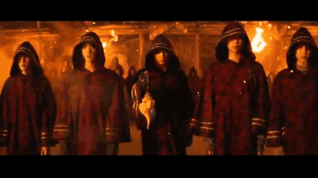 a group of people in red robes with hoods are standing in a line .