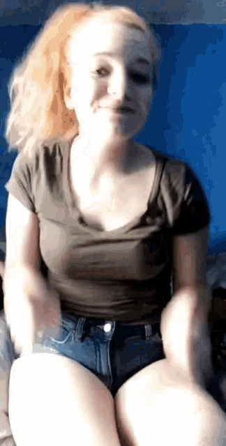 a woman wearing shorts and a t-shirt is sitting on a bed and smiling .