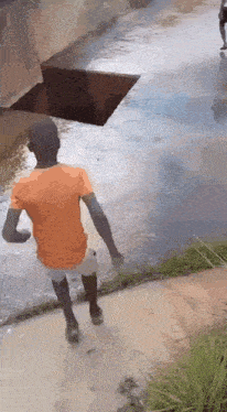 a man in an orange shirt is running through a muddy river .