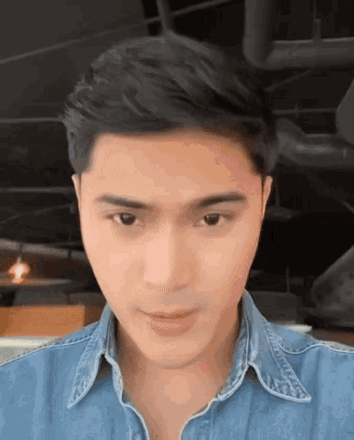 a close up of a man 's face wearing a denim shirt and looking at the camera .