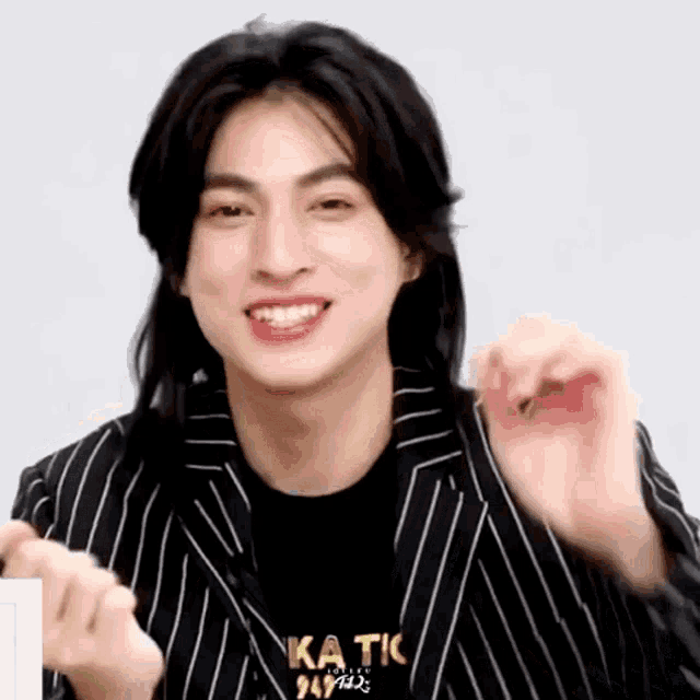 a man with long hair is wearing a striped jacket and a black shirt with the word katic on it .