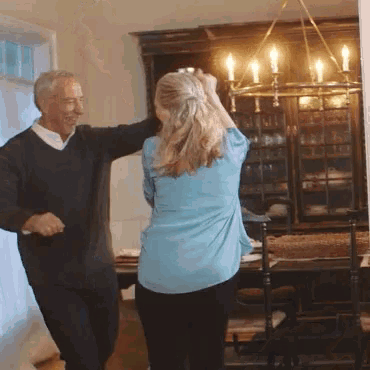 a man and woman are dancing in a room with a chandelier