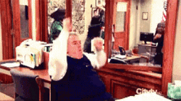 a man is sitting at a desk with his arms up in the air .