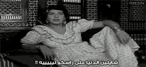 a woman in a white dress is sitting on a couch in a black and white photo with arabic writing on it .