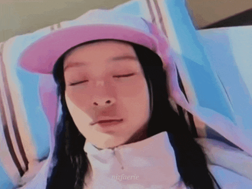 a woman wearing a pink hat and a white jacket is laying in a bed with her eyes closed .