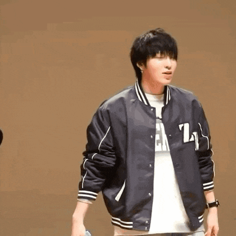 a young man wearing a black baseball jacket is standing on a stage .