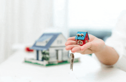 a person is holding a small model house and keys