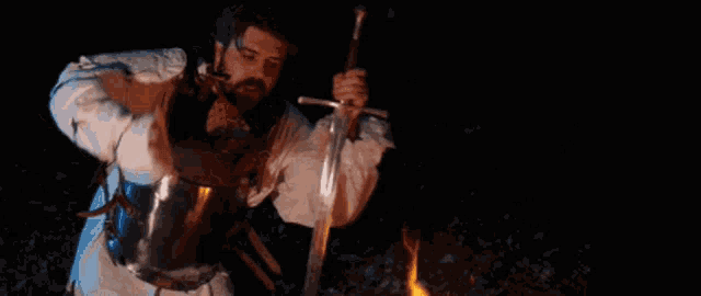 a man in armor is holding a large sword in front of a fire