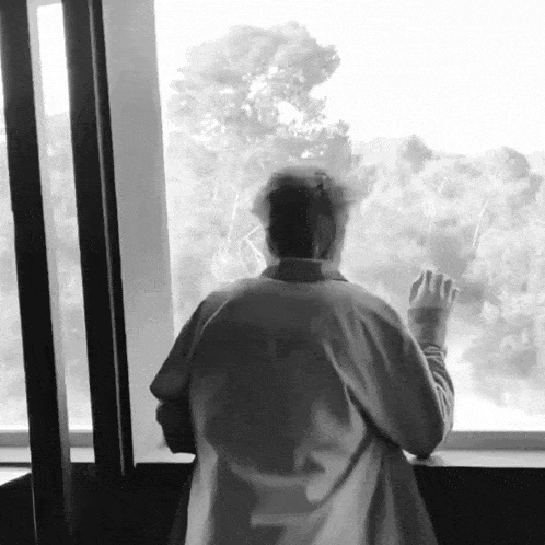 a man is standing in front of a window and looking out .